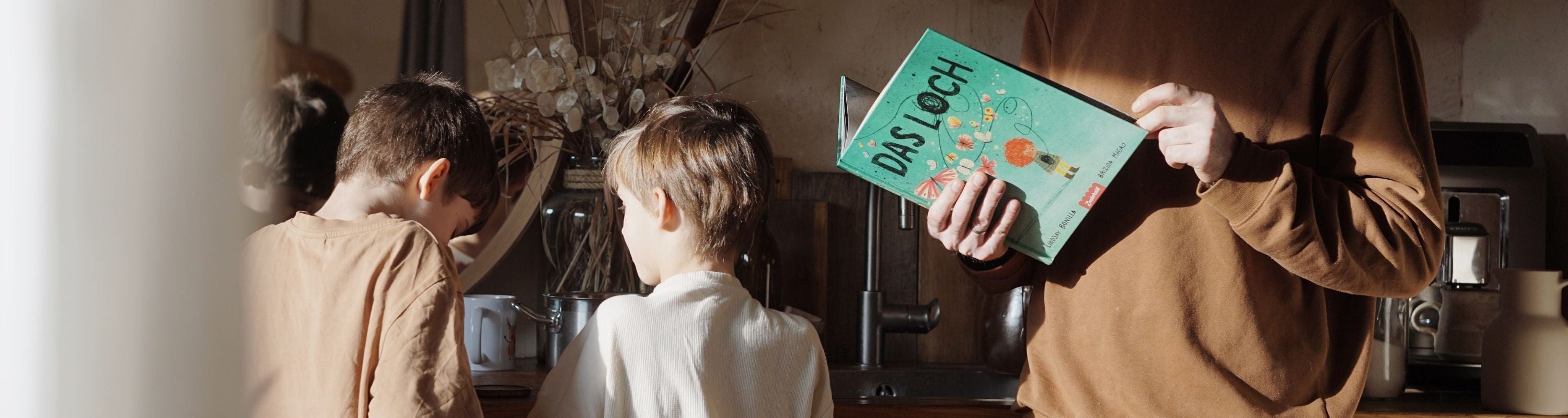 Ein Erwachsener liest neben zwei Kindern "Das Loch"