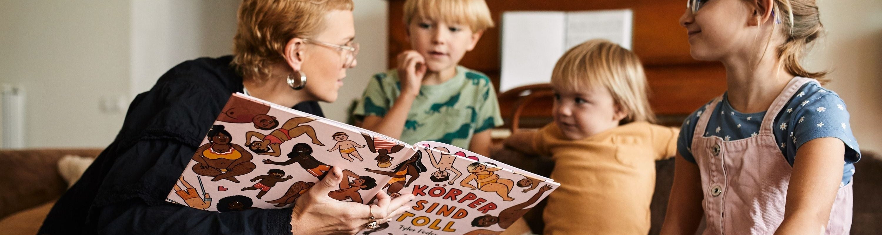 Eine Erwachsene liest drei aufmerksamen Kindern, die um sie herum in einem gemütlichen Raum mit einem Klavier im Hintergrund sitzen, ein buntes Bilderbuch mit dem Titel Körper sind toll vor.