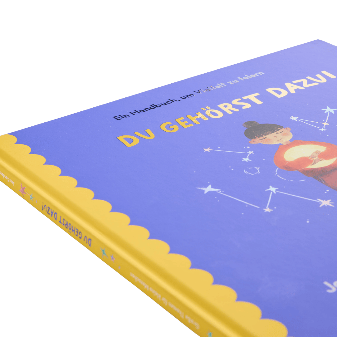 Eine Nahaufnahme von „Du gehörst dazu!“ vom Zuckersüß Verlag, einem deutschen Kinderbuch, dessen violetter Einband eine Illustration zeigt, auf der ein Kind ein leuchtendes Herz in der Hand hält, umgeben von Sternbildern. Dieses Bilderbuch setzt sich auf einfühlsame Weise mit den Themen Vielfalt und Zugehörigkeit für junge Leser*innen auseinander.