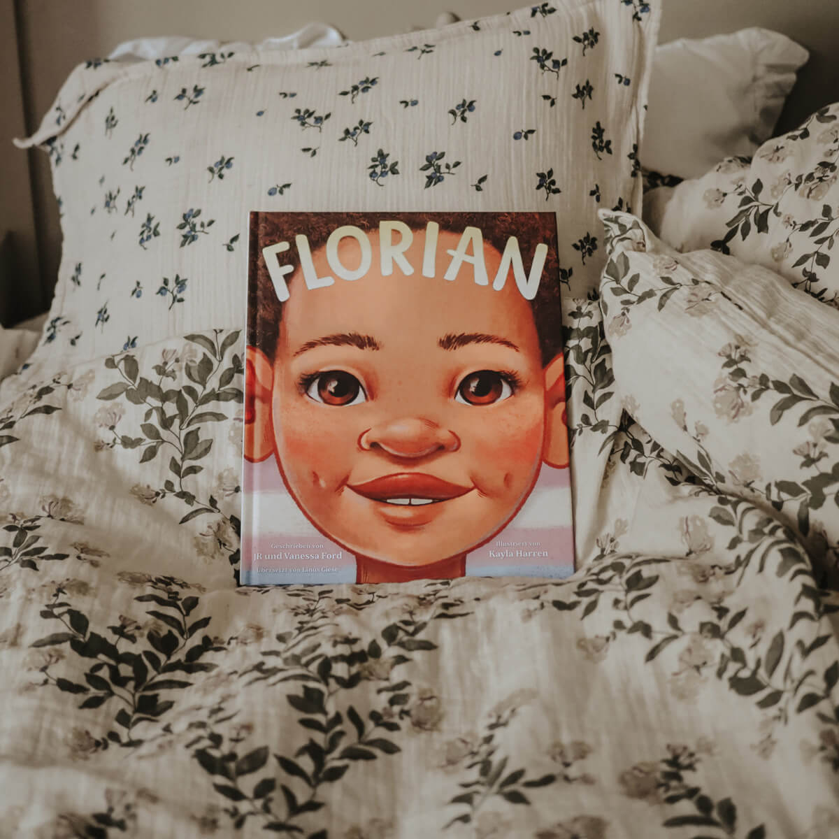 "Florian" von JR Ford & Vanessa Ford, ein identitätsstiftendes Kinderbuch, zeigt ein illustriertes Kindergesicht, das auf einem weiß-grün geblümten Bettzeug mit Kissen ruht.