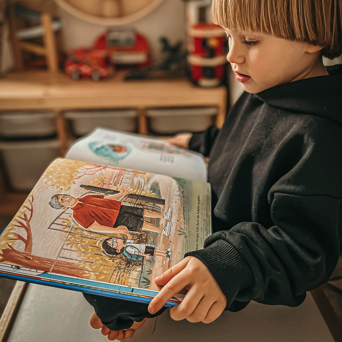 Ein Kind in einem schwarzen Kapuzenpulli sitzt in einem Haus und liest das Buch