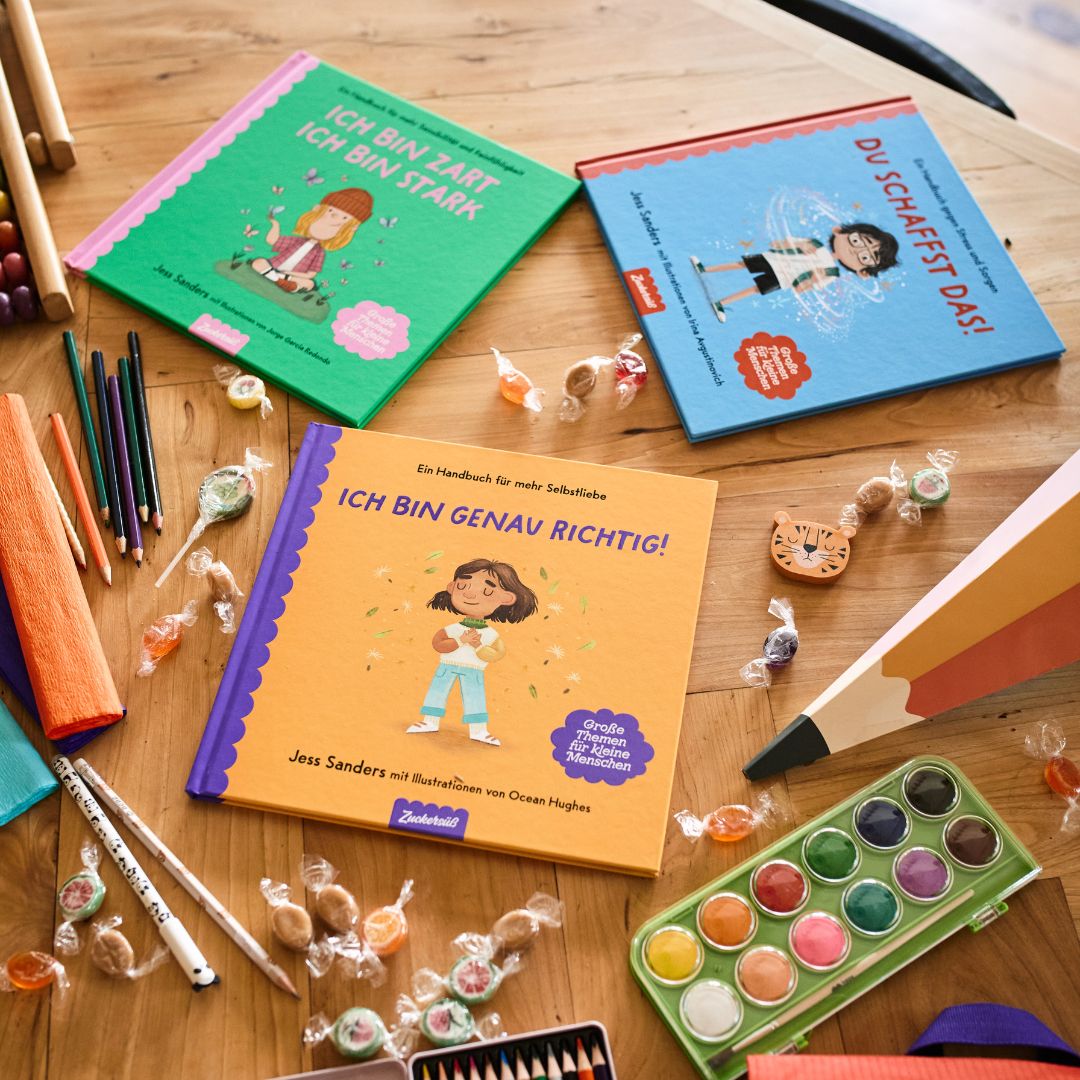 Das „School Starter Pack“ des Zuckersüß Verlags enthält drei farbenfrohe Bücher zum Thema „Schulstart“, die zusammen mit Bleistiften, Wasserfarben und Süßigkeiten dargestellt sind – eine kreative Szene, die Kindern auf ihrem Weg zur Einschulung Selbstvertrauen vermittelt.